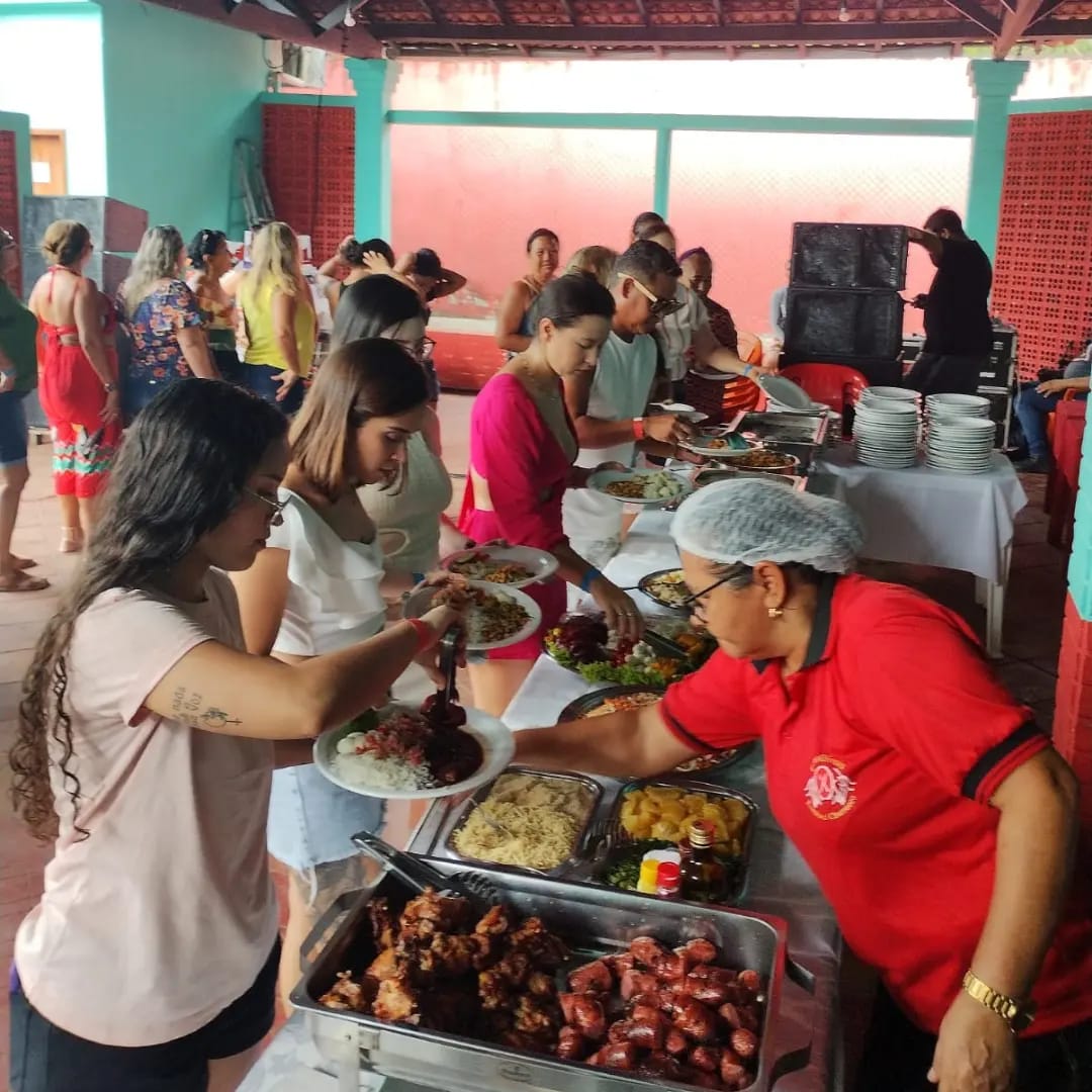 buffet de evento com funcionária de camisa vermelha servindo comida em bandejas para convidados em um salão co
